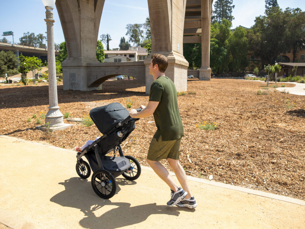 A man jogs through a park with his Ridge jogging stroller. 