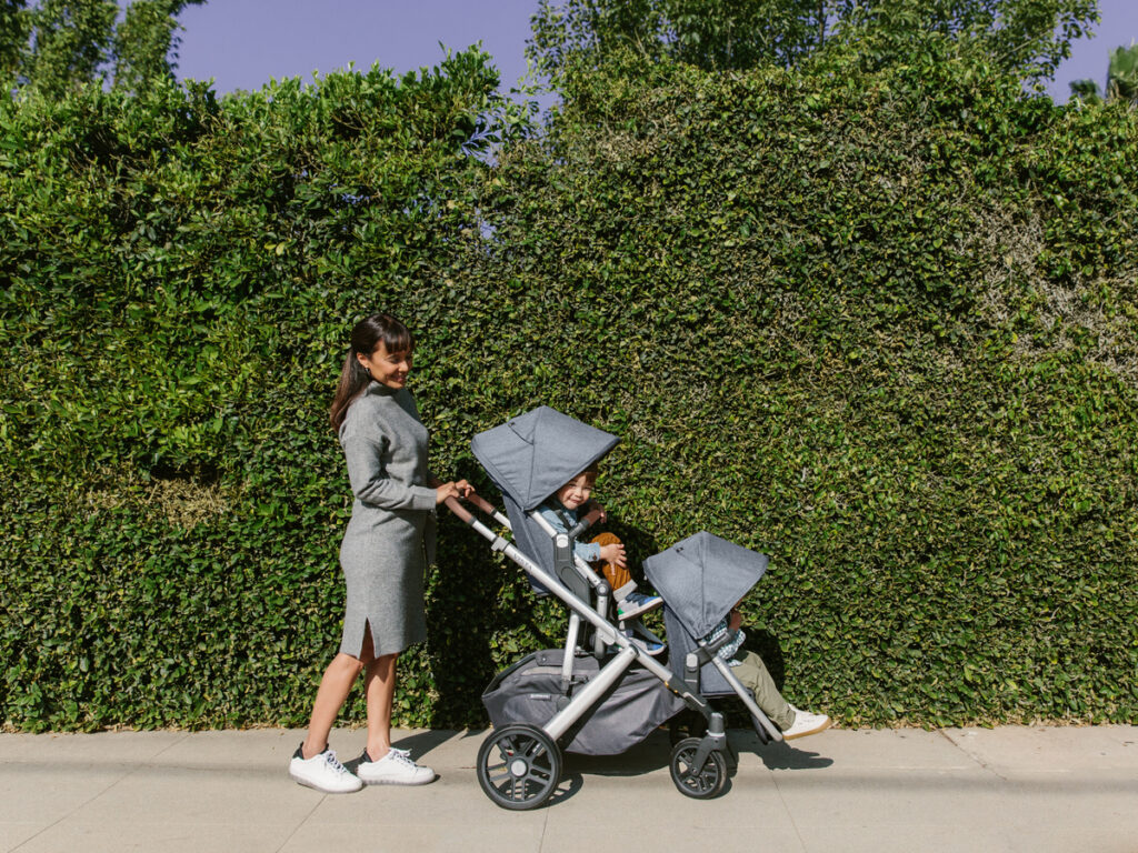 A woman strolls with her two children in a double Vista along a green path. 