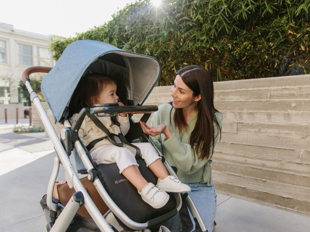 Mother smiles at child secured strapped into the Vista V2 with attachable snack tray. 