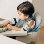 Baby sitting in Ciro High Chair with attached Cushion while eating sliced bananas