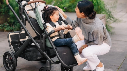 Parent enthusiastically looking at two children in forward facing RumbleSeat V2+ and Toddler Seat in Gwen fashions attached to Vista Stroller