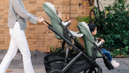 Parent pushes two children in Gwen Vista with forward facing RumbleSeat V2+ (lower) and Toddler Seat (upper)