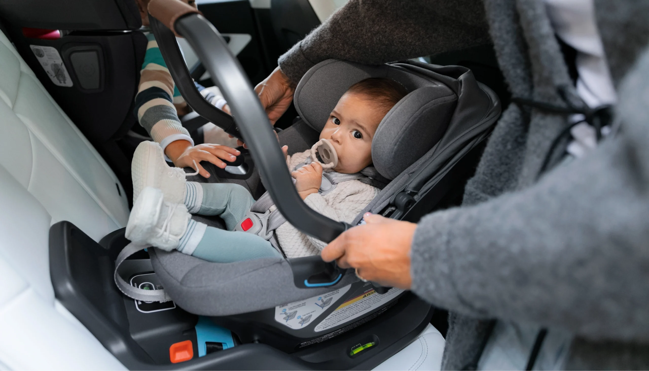 A child safely installed in an Aria car seat with her caretaker deploying the 5th anti-rebound handle position for increased safety in rebound and rear-impact collisions