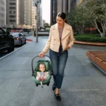 A woman effortlessles carries her child down a city sidewalk due to Aria's lightweight build and ergonimic aluminum carry handle designed for stability and ease of portability