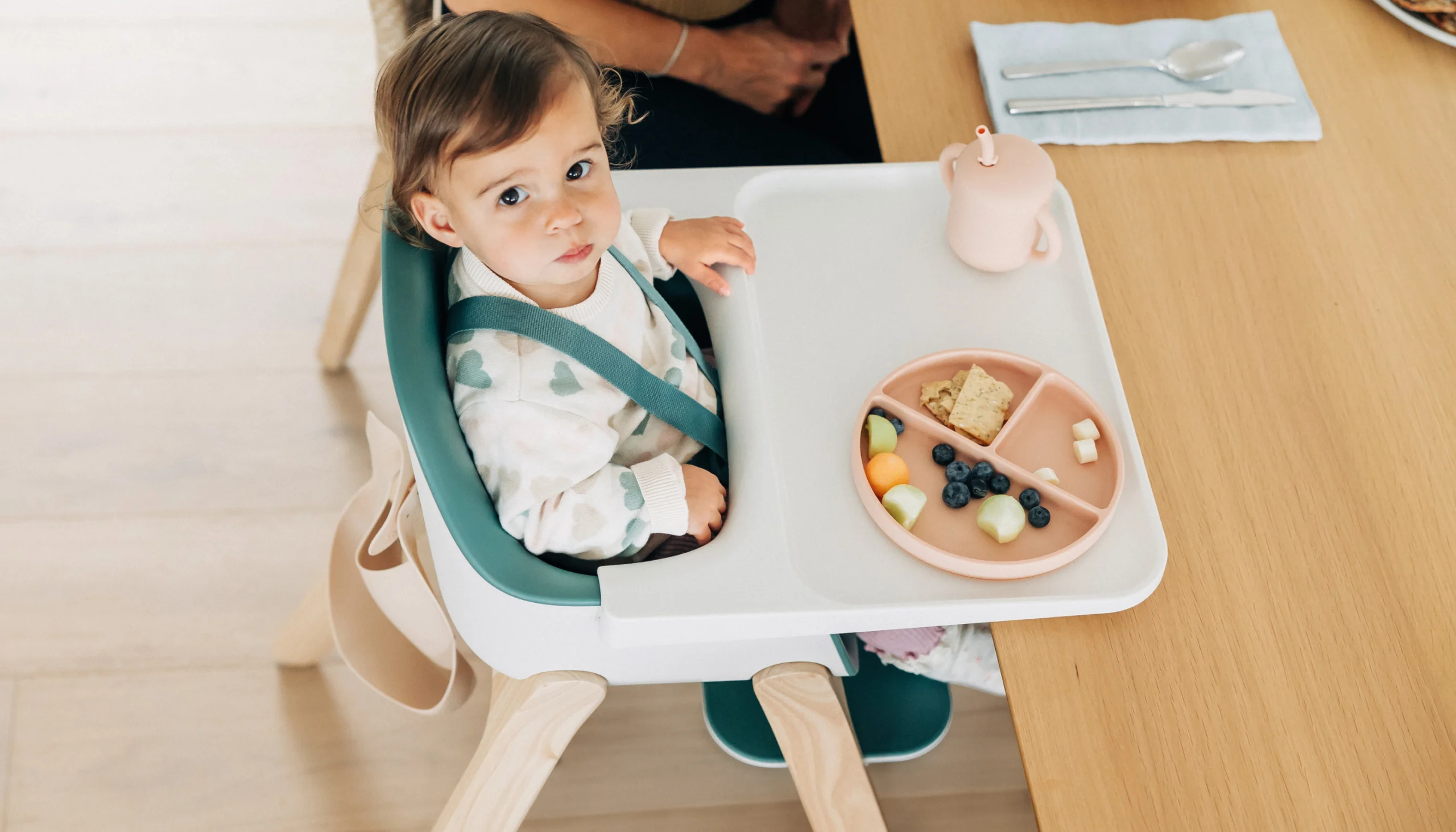 Baby looks up as he is sitting in the Ciro high chair enjoying a meal at the table with others