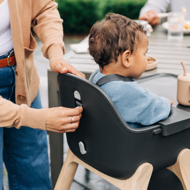 Getting ready for meal-time, a woman grabs babay's bib, conviniently clipped to the Bib hook located at the back of the seat for simple storage when not in use