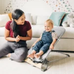 A smiling toddler comfortably sits in the Mira 2-in-1 bouncer, staying cool with its dual comfort seat and breathable mesh