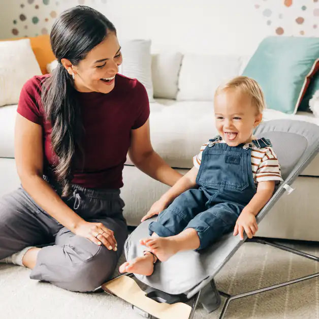 A smiling toddler comfortably sits in the Mira 2-in-1 bouncer, staying cool with its dual comfort seat and breathable mesh