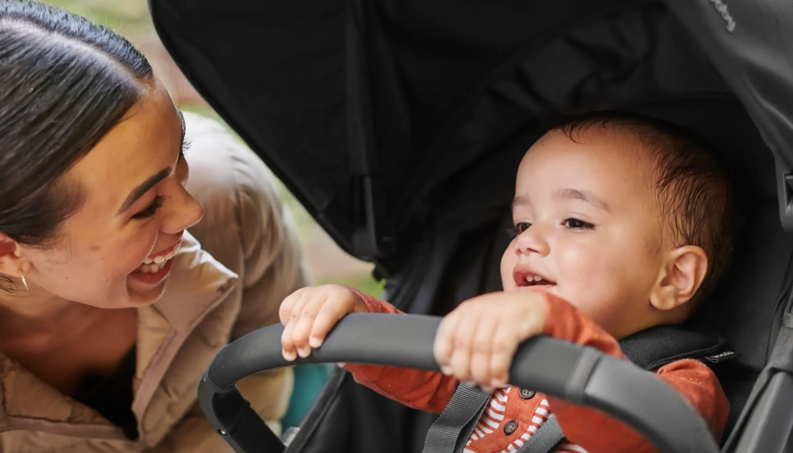 Mom smiling at child in Ridge stroller holding neoprene cover on Ridge Bumper Bar for added comfort for child