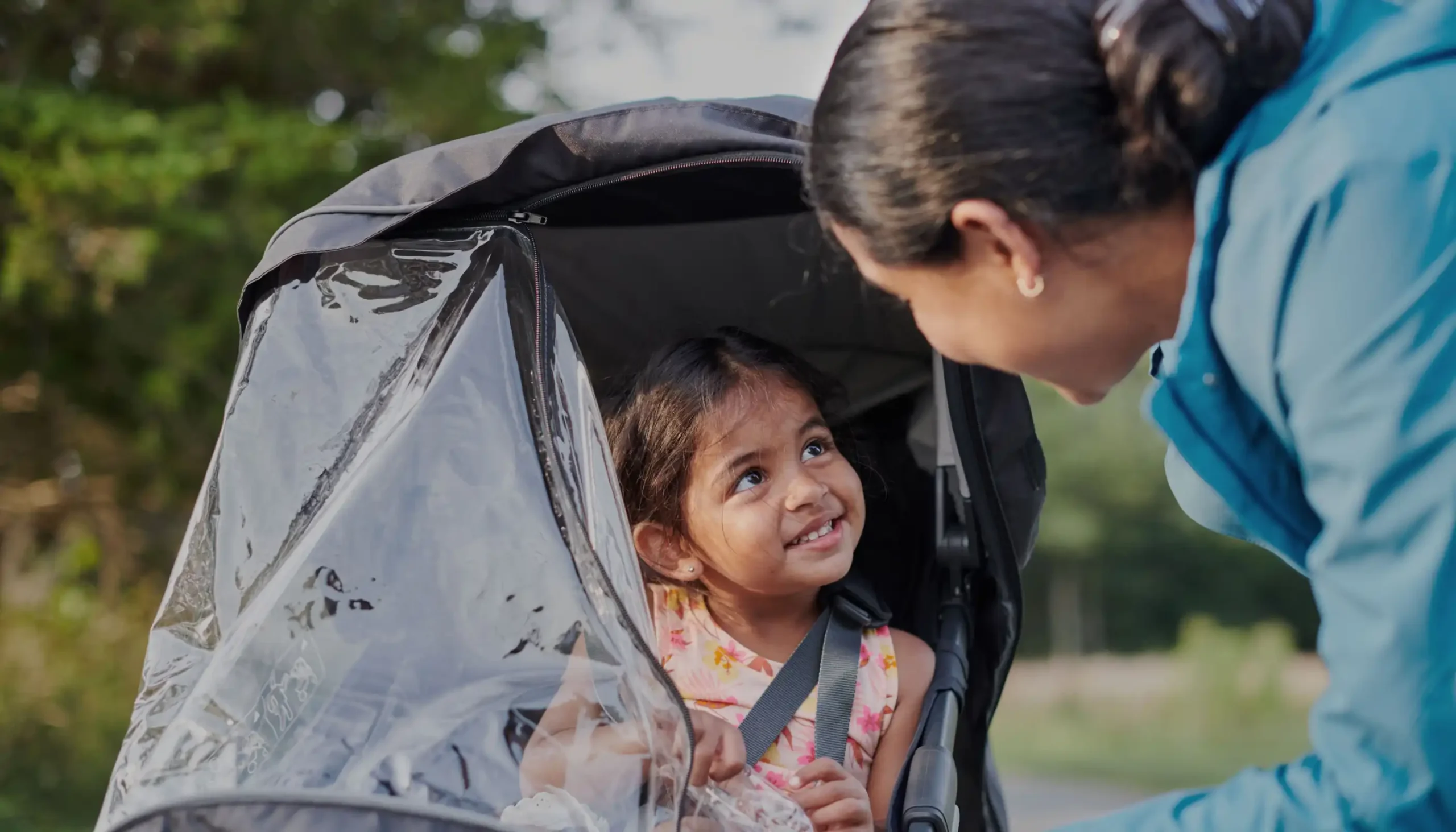 Child sitting in Ridge stroller smiling at parent unzipping Performance Rain Shield window opening