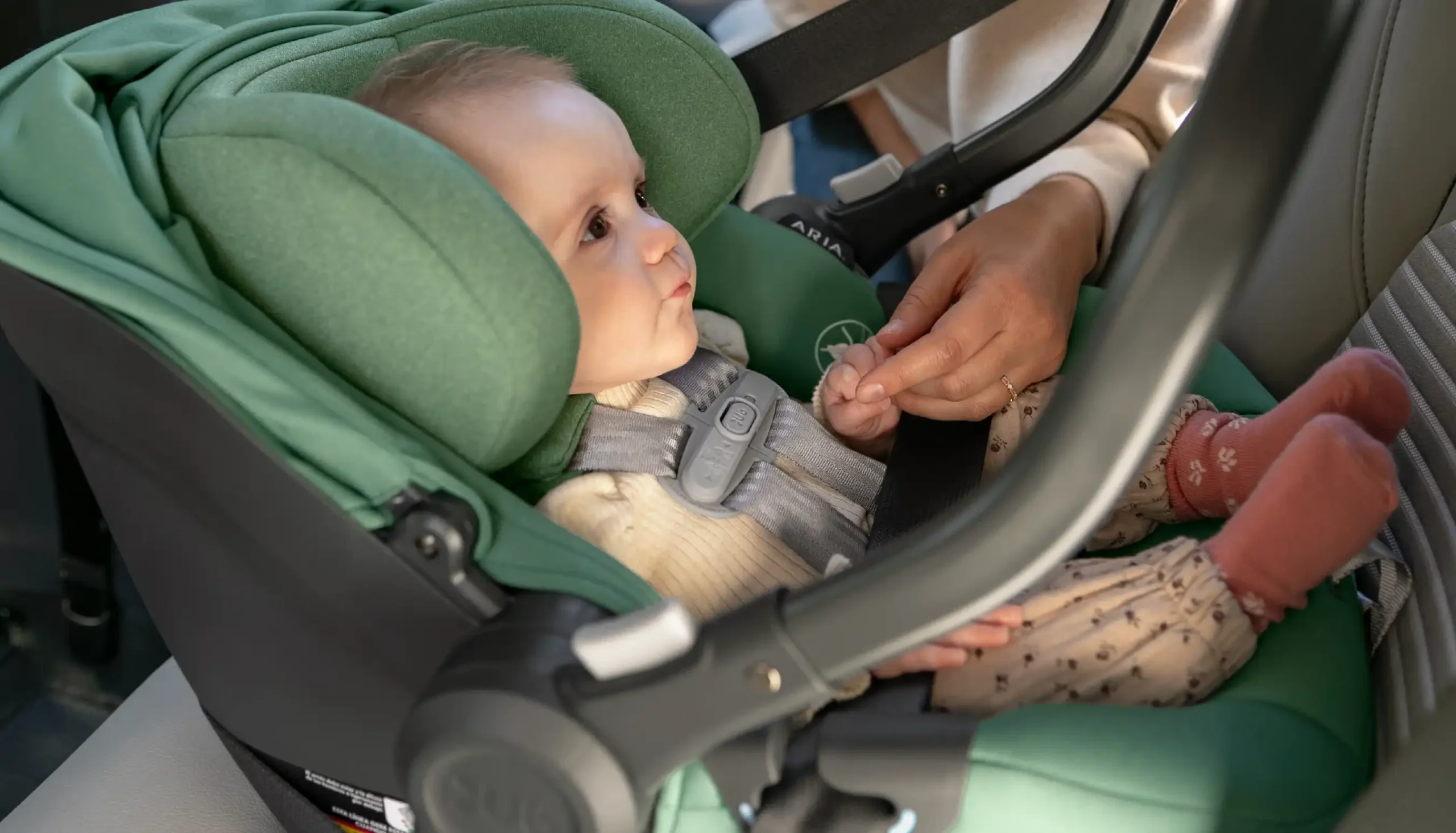 Baby holds mothers hand while securley strapped into the Gwen Aria carseat