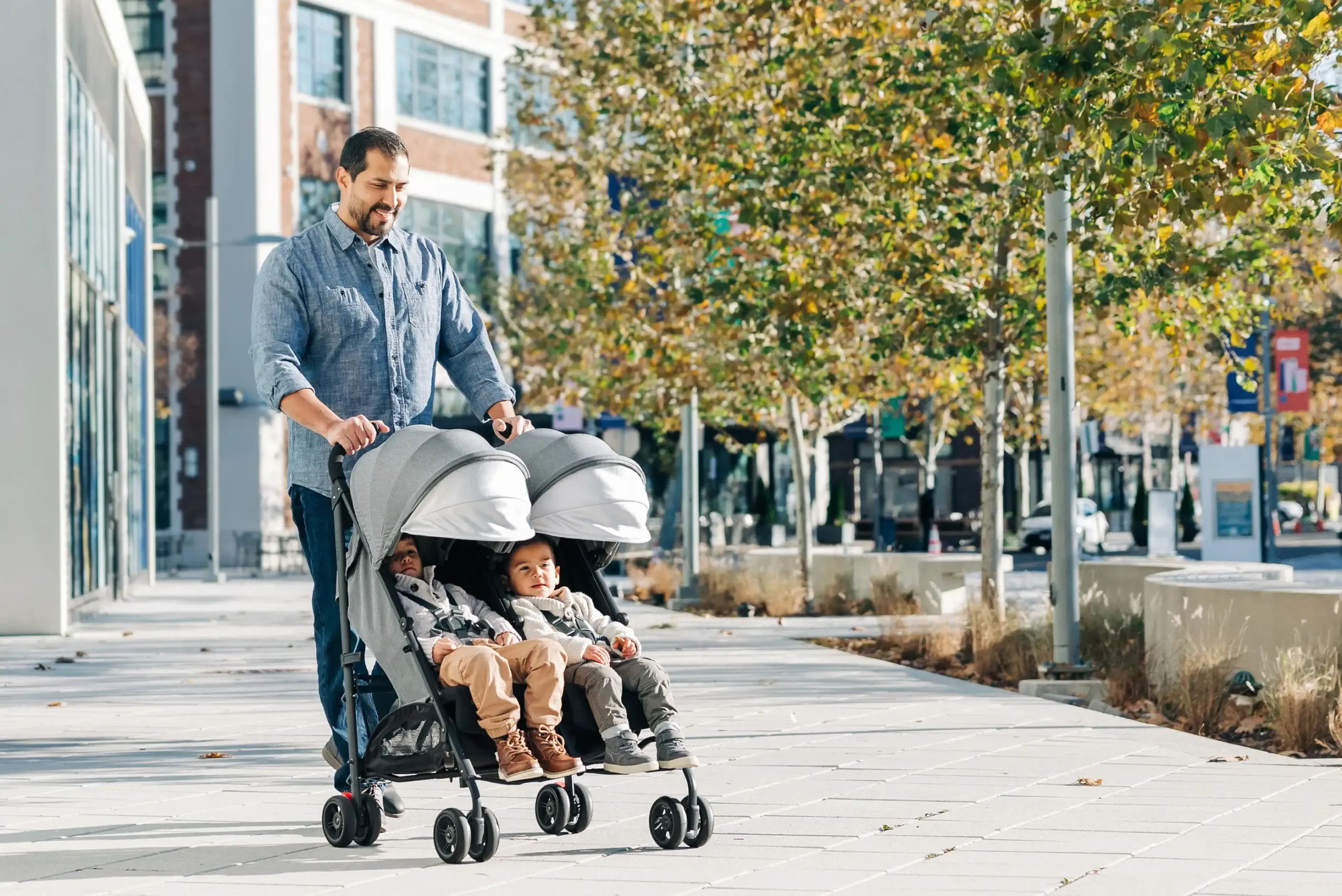 A smiling father strolls with two children comfortably sitting side-by-side in the G-Link V2 thanks to its multi-position reclining seats and extendable UPF 50+ sunshade