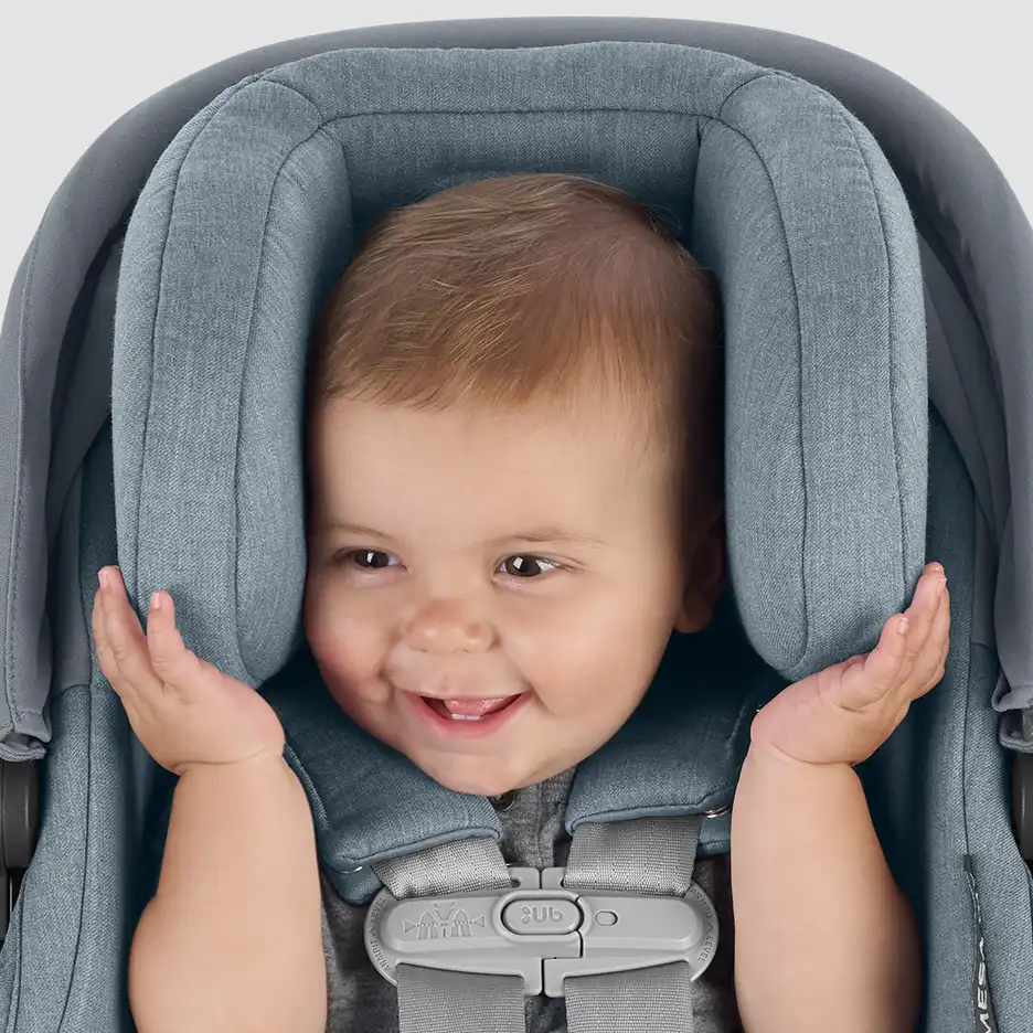 Infant sitting in car seat with correct headrest and harness placement. Baby is seen smiling while holding car seat showing the comfort and safety of the fit.