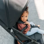 A toddler holds onto the 100% full-grain leather bumper bar while smiling in the Minu V2 stroller that holds up to 50 lbs.