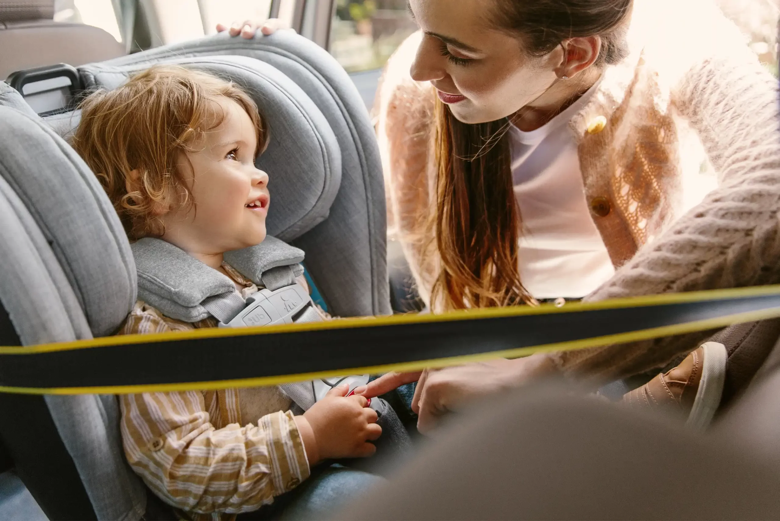 A child in the Knox Convertible Car Seat looks to a woman smiling, while he is safely installed with Knox's rear and forrward facing multi-direction tether to reduce seat rotation and stress on the child head/neck upon impact