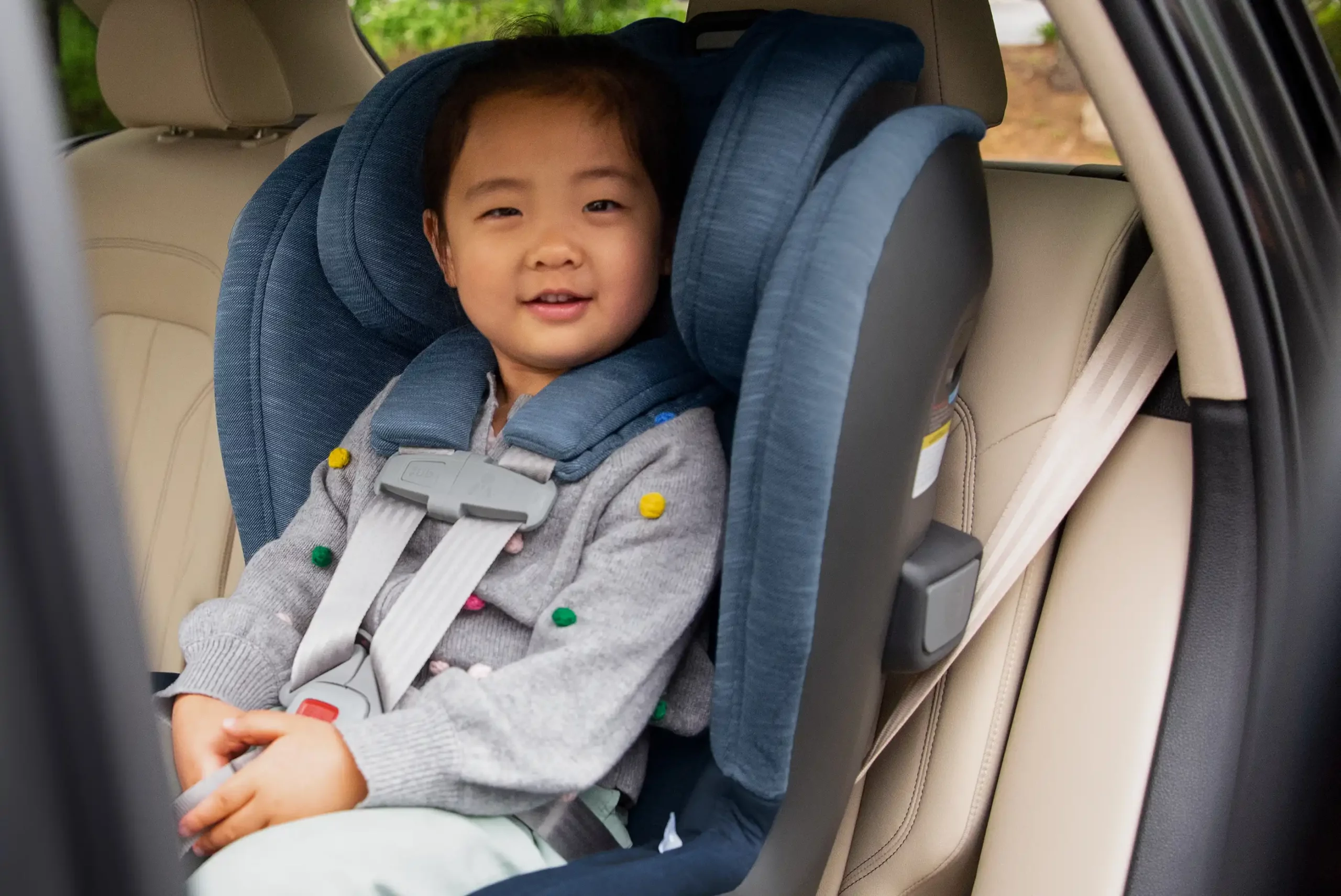 A child smiles at the camera in the Knox Convertible Car Seat, while safely installed using Knox's no-rethread harness and 8 position headrest for a precise fit