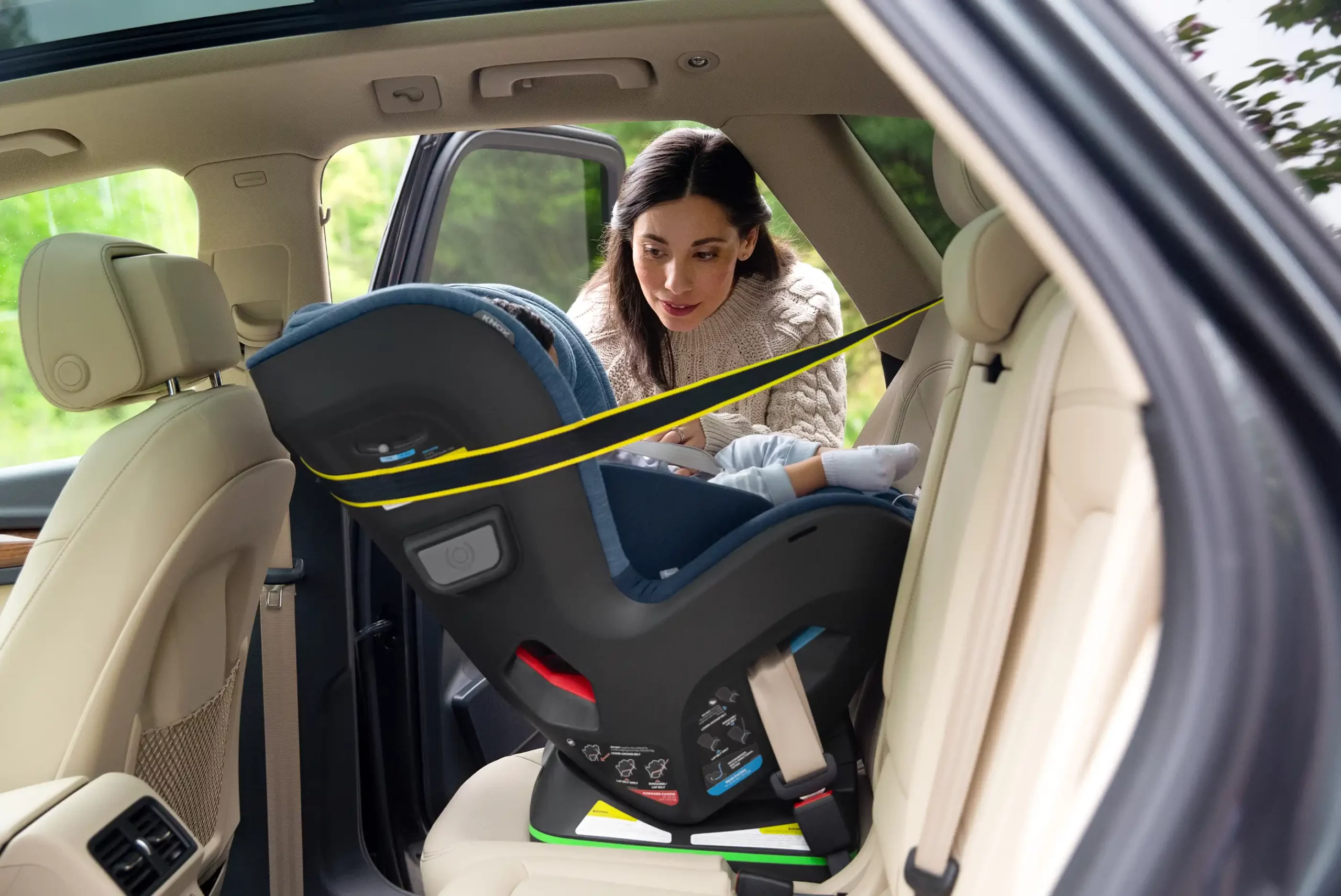 A woman smiles at her child installed in a rear-facing position in the Knox Convertible Car Seat, safely secured with Knox's multi-directional tether and side impact pods to deflect crash forces