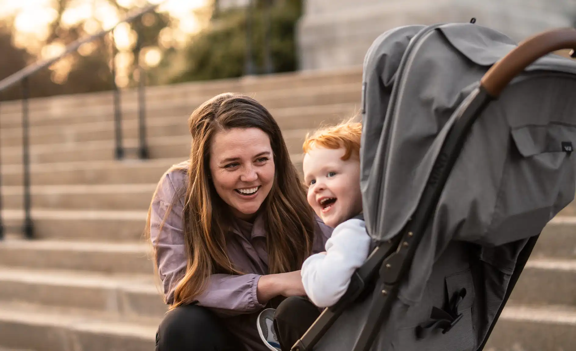 A mother smiles at child who is contently sitting in the Minu V2 lightweight stroller.