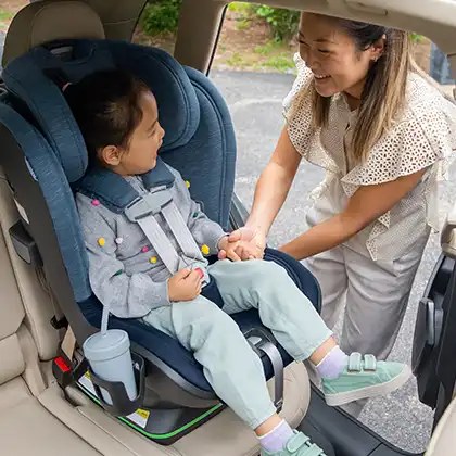 Mom smiling and holding the hand of young smiling child securely seated in car seat