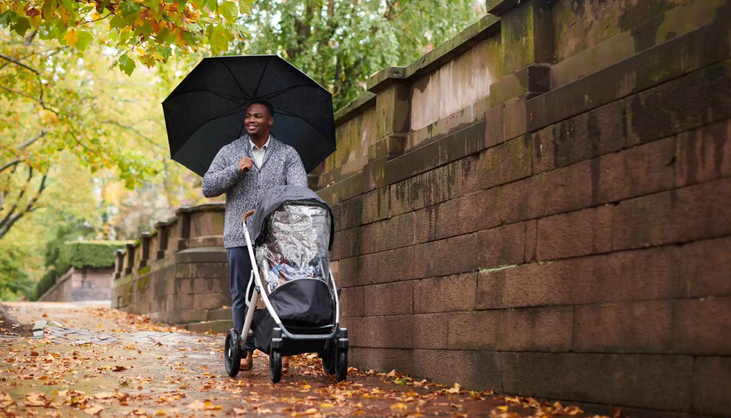 Parent smiles holding umbrella while protecting child from wind and rain with Performance Rain Shield attached to Vista/Cruz stroller